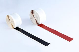 Two rolls of mastic tape on a white background. One unwinds a black strip, the other a red strip, each backed by a pale release liner.